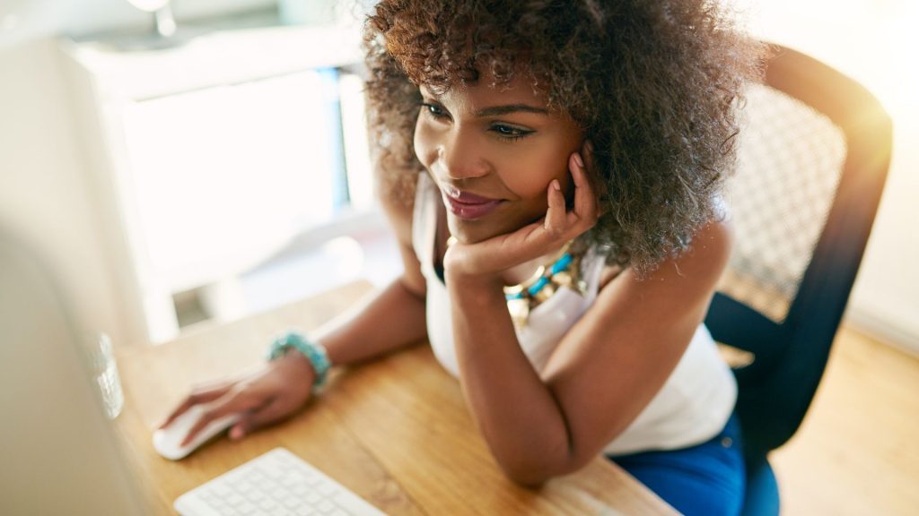 Brown skin woman with curly hair sitting at computer desk doing work