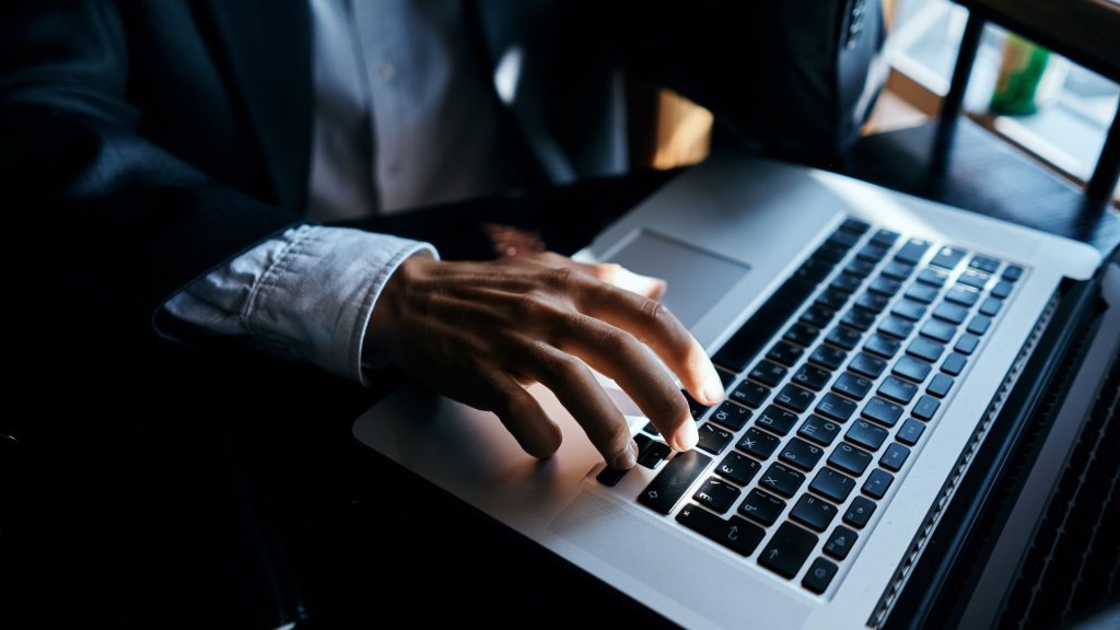 Hands of a Black professional man wearing suit typing on laptop keyboard