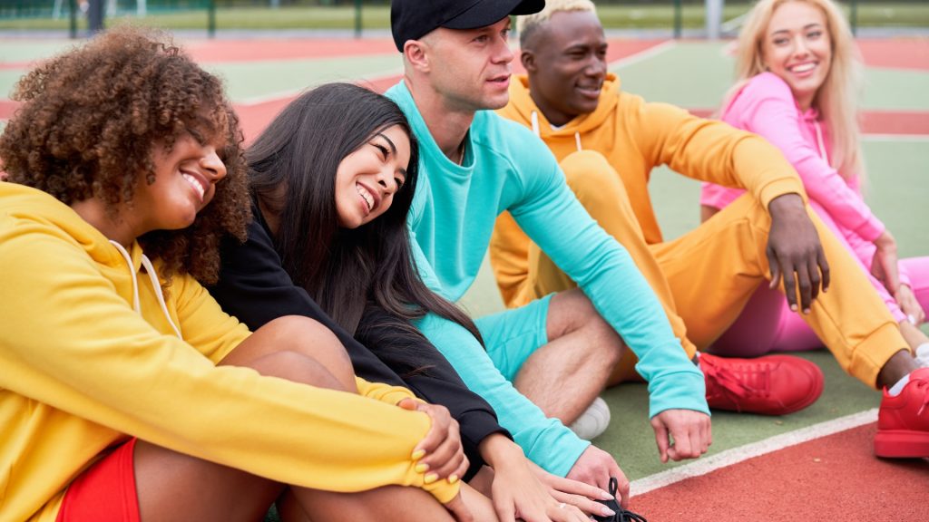 Diverse group of friends in colorful streetwear sitting on the ground of an empty playground