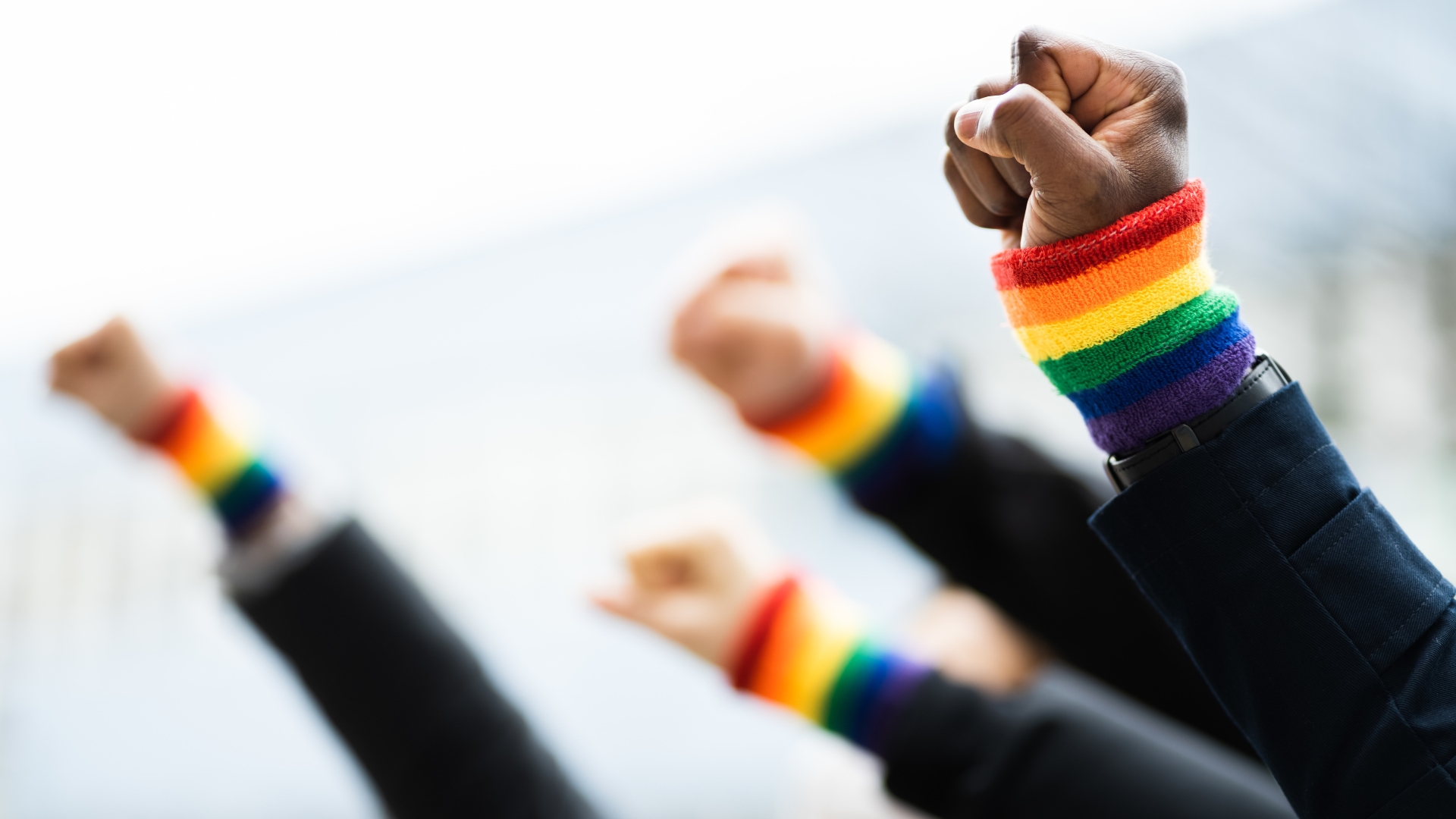 Several hands of LGBTQIA+ people holding their hands up in fists of solidarity to celebrate Pride month.