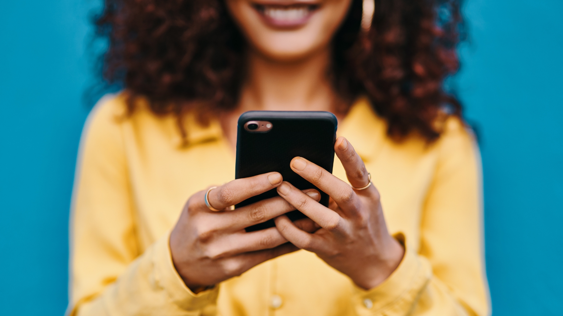 Black woman with brown curly hair wearing a yellow blouse holding her cell phone