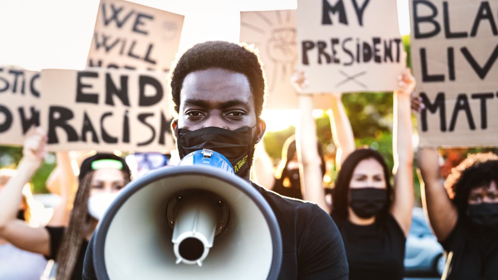 A group of young Black activists standing in the streets and speaking out about racial inequality and injustice.