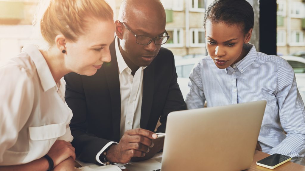 A diverse group of executives sitting behind a laptop working on an important project.