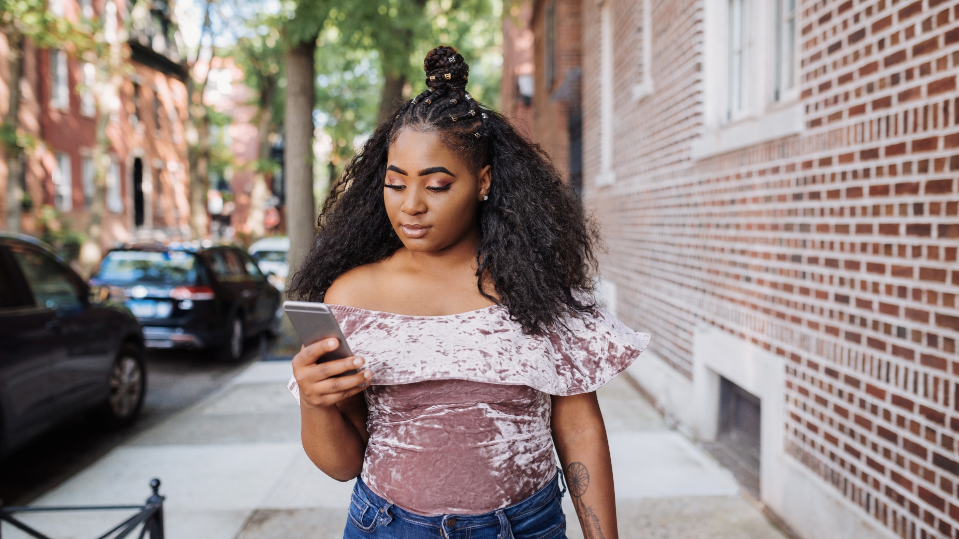 African American Gen Z young woman with curly hair and a velvet halter top looking at her phone attentively