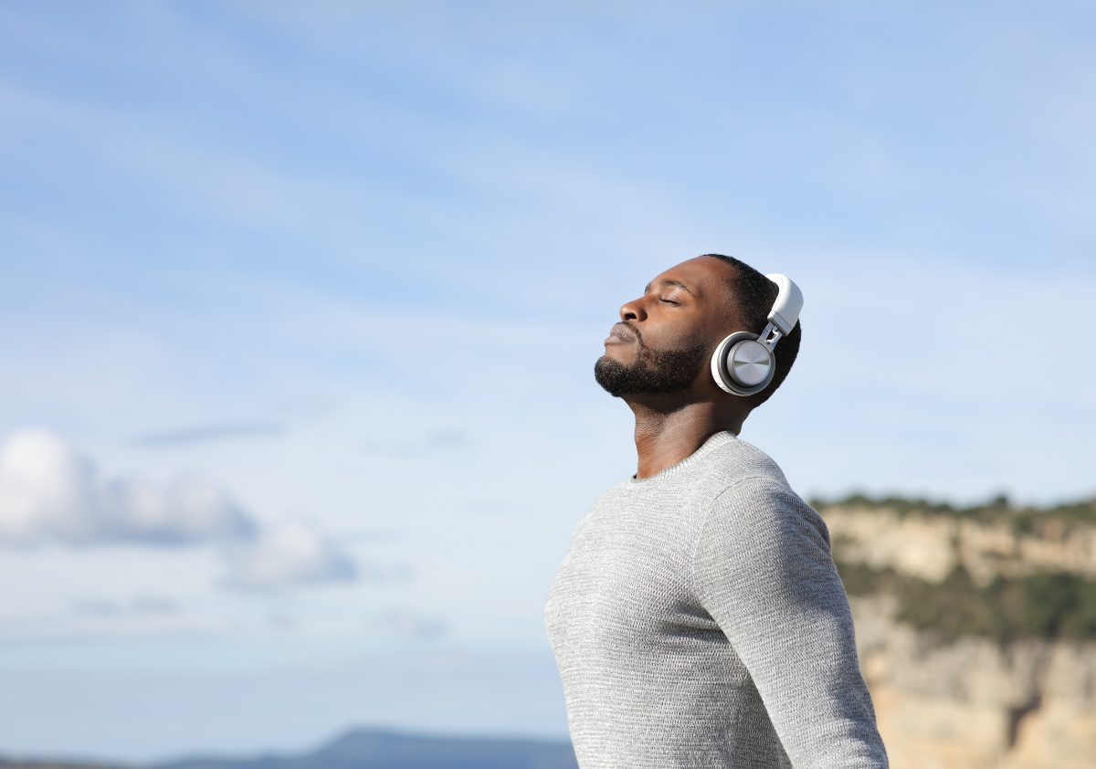 Fit Black man wearing headphones stands on top of a mountain breathing in fresh air