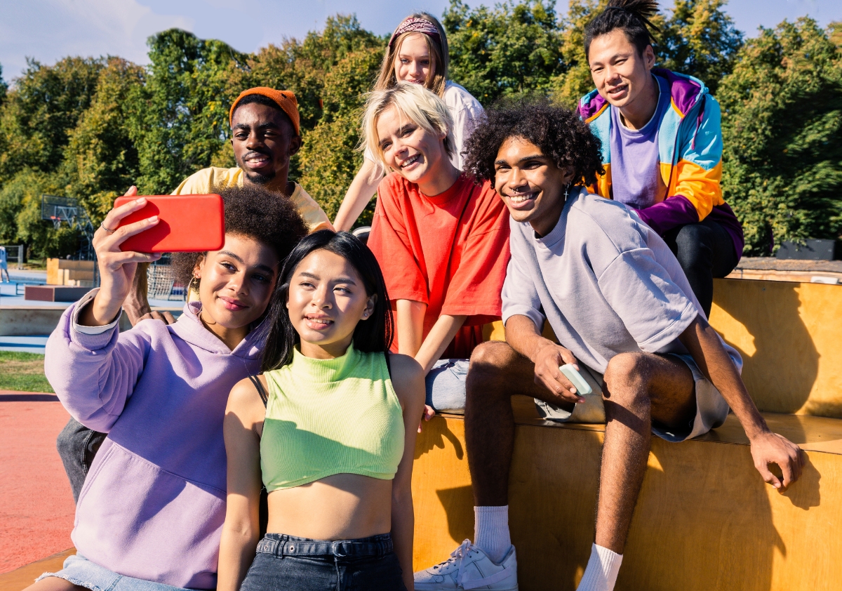 A group of diverse multiracial millennials wearing brightly colored activewear taking selfies together in a park.