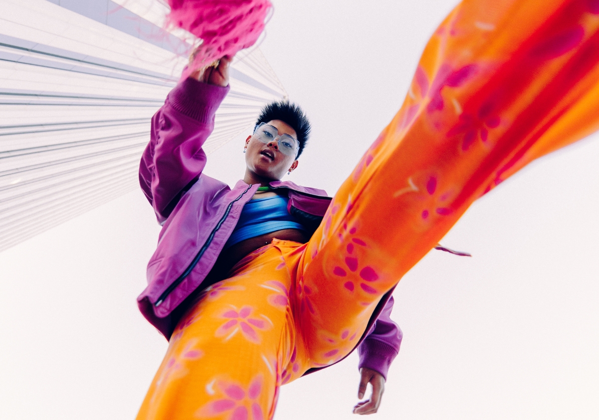 A multicultural TikTok influencer dressed in bright purple jacket and bright orange floral print pants showcasing a cultural trend