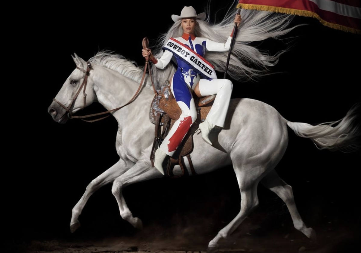 The Cowboy Carter album cover; Beyonce wearing American Flag bodysuit while sitting atop a white horse and holding the American flah