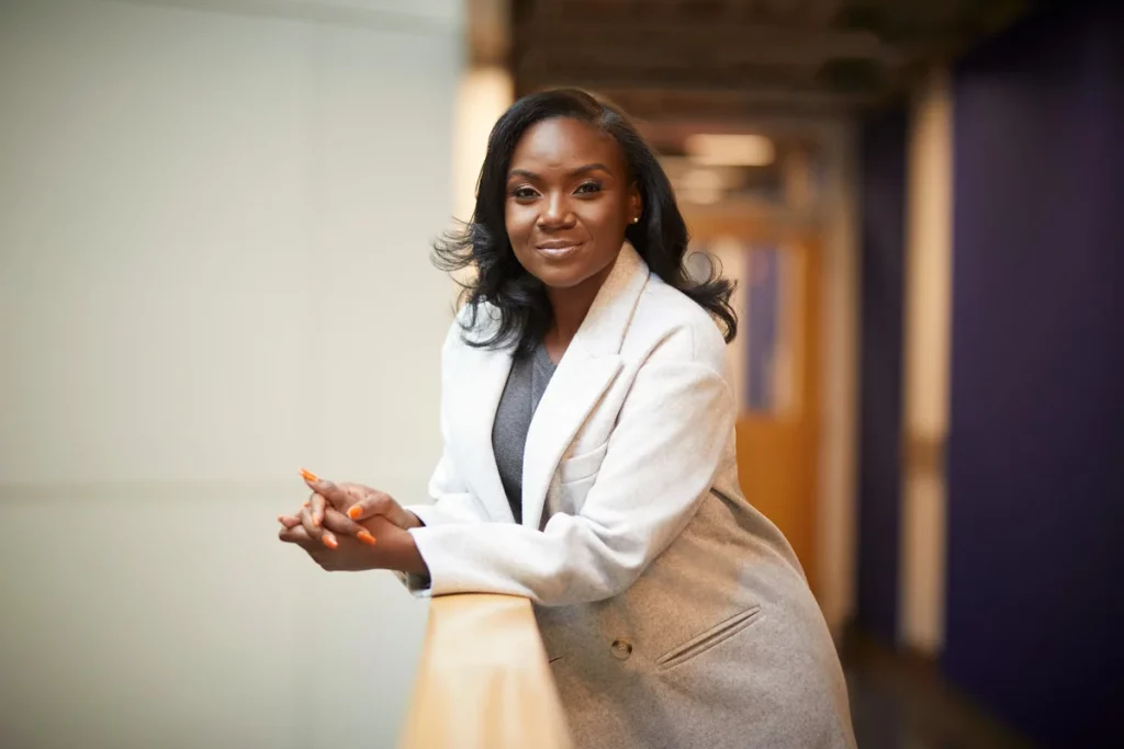 Black female immunoligist Dr. Kizzmekia Corbett wearing grey suit jacket and smiling for public health messaging
